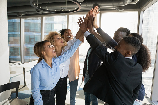 Overjoyed African American business people giving high five at meeting, standing in modern office, employees team colleagues celebrating sharing success, business achievement, team building activity