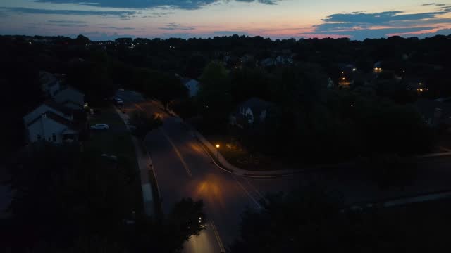 Car driving on American neighborhood road at night. Aerial establishing shot of houses and homes after sunset during dusk.