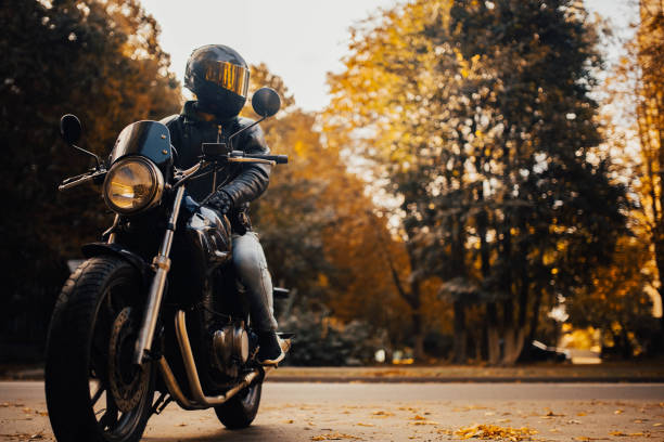 motocycliste dans un casque avec une moto classique à l’automne. motard élégant dans une veste en cuir et des gants. - moto photos et images de collection