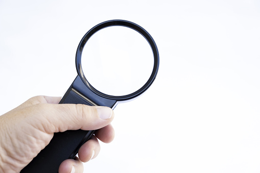 Human hand holding black magnifying glass on whithe background, closeup.