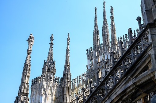 MIlan, Italy – June 18, 2023: Various columns with statues no top of the Milan Cathedral with blue sky background.