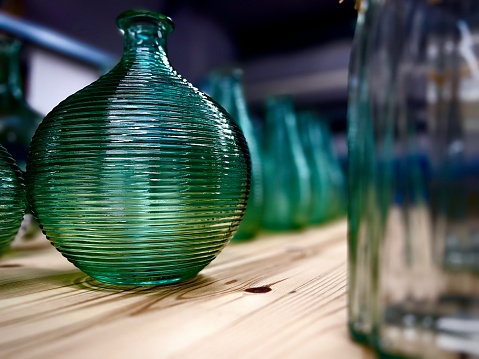 A green glass vase amongst other vases on a wooden shelf