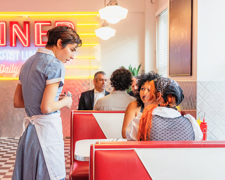 A woman talking to customers at a diner about the available options for food and drink.