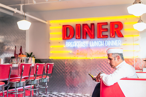 The owner of an empty diner sitting at a booth and checking his phone as he waits for customers.