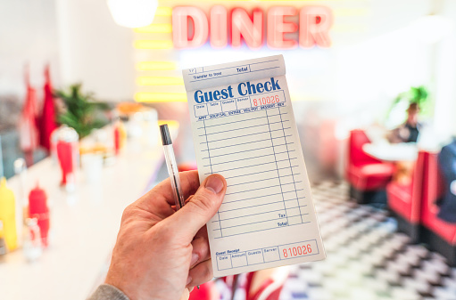 An employee's hand holding a pad of order sheets, ready to take food an drink orders in a traditional diner restaurant.