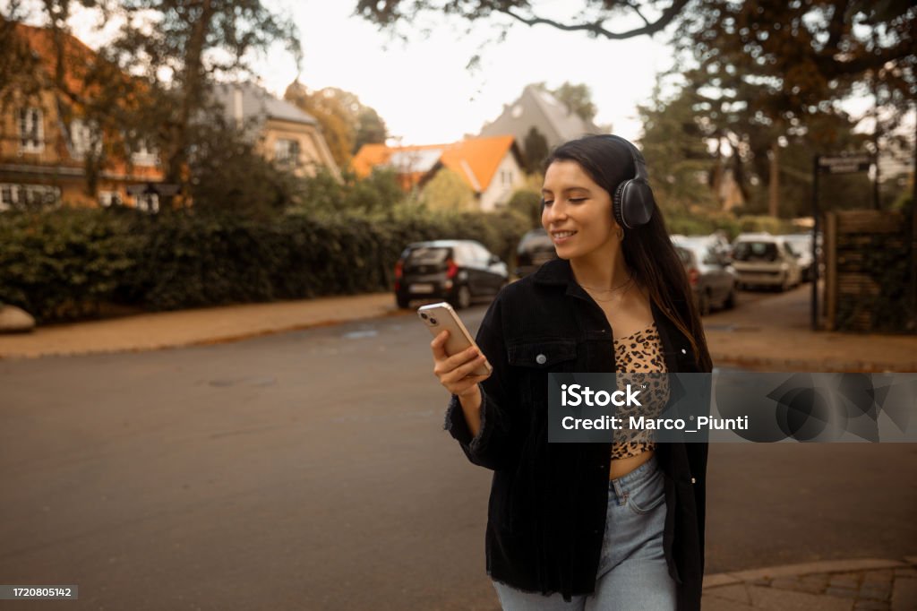 Young woman walking outdoor in the city street Young latin american woman portrait outdoor in the city street and using smartphone and wireless headphone 20-29 Years Stock Photo