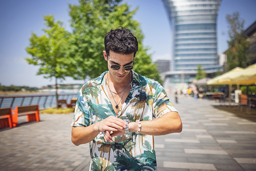 Portrait of a handsome modern man checking the time on wristwatch outdoors in city.