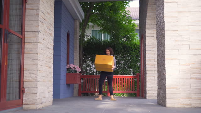 Woman walking to at front of her home to get package box from messemger that droped.