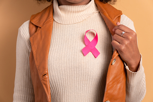 detail hands of african american woman showing pink ribbon in studio shot. breast cancer, awareness concept.