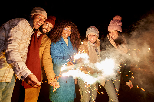 Group happy people lighted fireworks party at winter celebration with sparklers. Multiracial friends enjoying night outdoor having fun together. Christmas, wishes purposes new year vacation lifestyle.