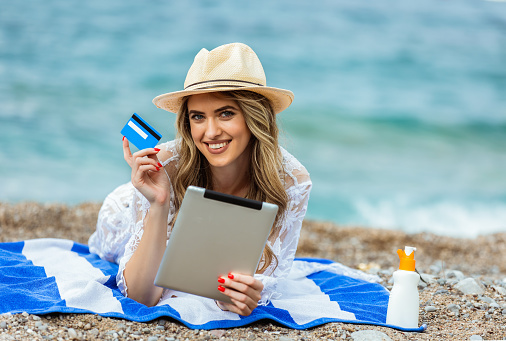 Young girl ordering something online whith the card, while lying on the beach
