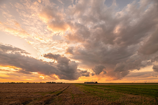 Clouds over the wide open plains are colorfully illuminated by the rising sun.