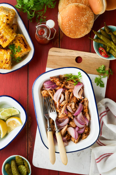 istock Pulled bbq chicken with baked onions on serving platter, bbq corn, pickles, chili peppers and buns for hot dogs and burgers, tomato sauce. Traditional American grilled summer bbq sandwiches dishes. 1720935383