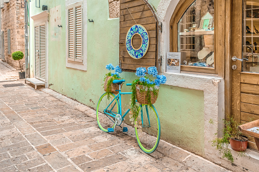 Budva, Montenegro - June 17, 2021: Bright lime-blue bicycle with wicker baskets with blooming hydrangeas at the entrance to a souvenir shop in Budva Old Town. Vintage atmosphere on a medieval street