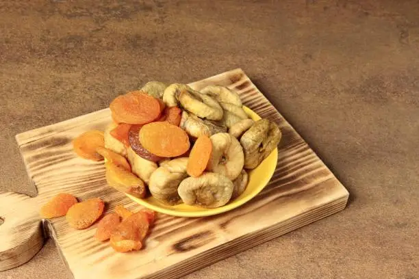 Photo of Dried figs, dried apricots on a yellow saucer on the table.