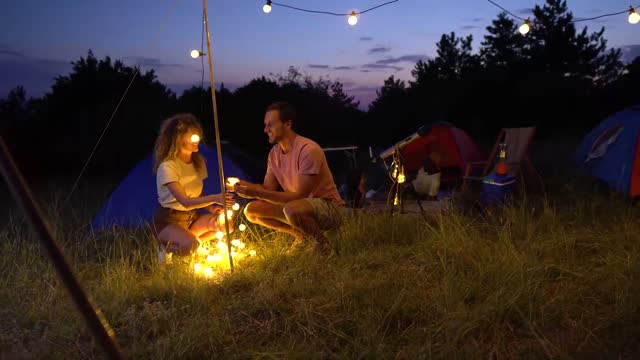 Young couple setting up string lights to decorate and lighten their camping spot at night