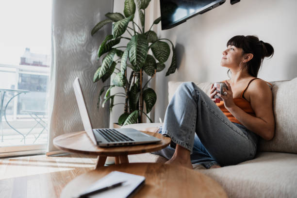 Young woman drinking coffee and looking through the window at apartment