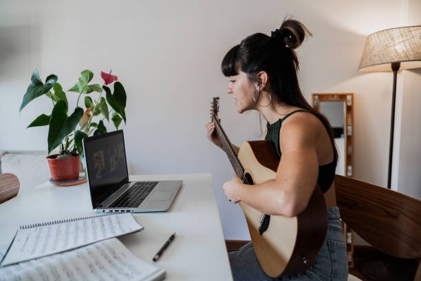 молодая женщина по видеозвонку учит игре на гитаре дома - 20s acoustic guitar adult attractive female стоковые фото и изображения