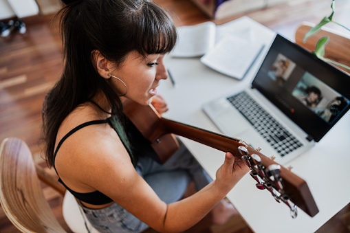 Young woman on a video call teaching guitar in the apartment