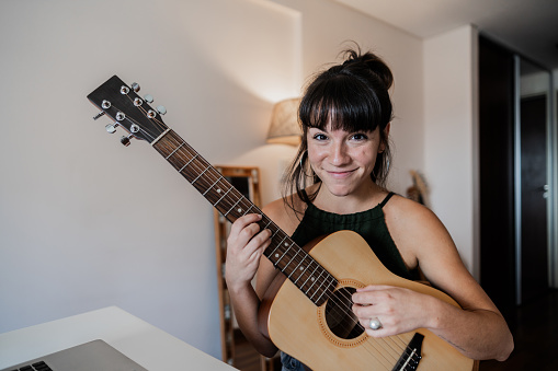 Portrait of a young woman playing the guitar in the apartment