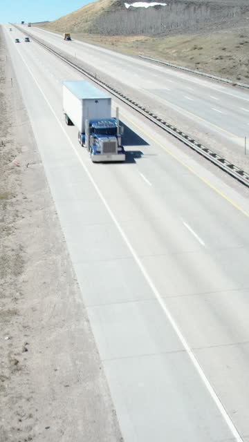 A Vertical Drone Shot of a Semi Truck Passing By on a 4 Lane Highway in Northern Utah on a Clear Spring Day