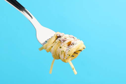 Fork with tasty pasta on light blue background, closeup