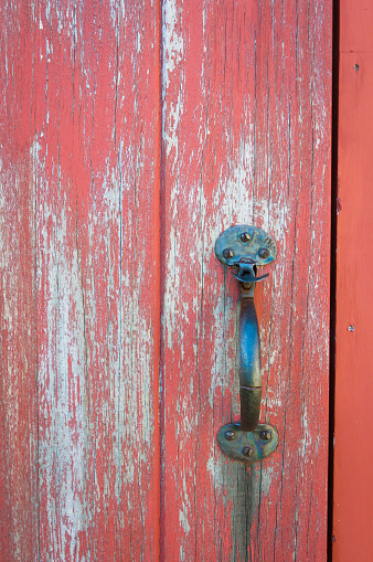 An antique iron door latch on a red door with worn peeling paint.