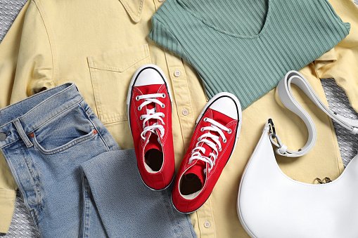 Pair of stylish red sneakers, clothes and bag on light grey fabric, flat lay