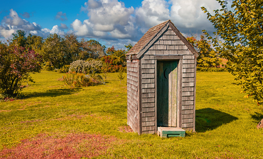 A rustic outhouse rests in a grassy field on a Cape Cod farm on an October afternoon