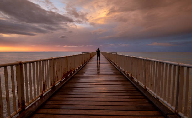 istock Person standing alone on a pier enjoying dramatic sunset at the sea. Exploring nature 1721189396