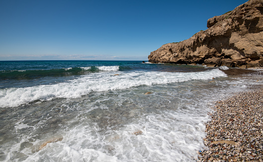 Empty pebble tropical beach under white cliffs against blue sky. Copy space