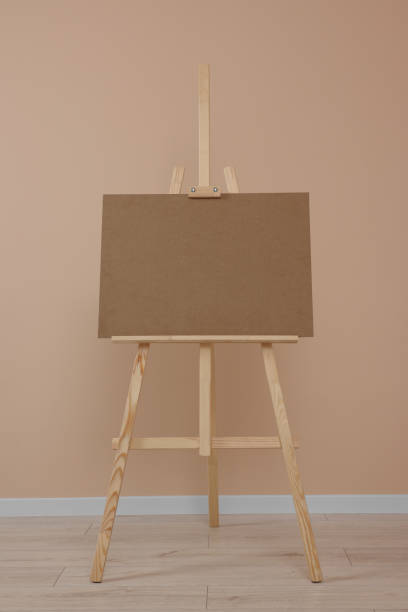 istock Wooden easel with blank board near beige wall indoors 1721189422