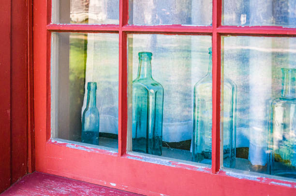 Antique dusted bottles displayed on the rustic weathered window with the view of tree trunk and branches leaves, an image for memories, nostalgia, good old times, or lonesomeness