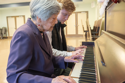 Teenaged volunteer playing piano with 90+ Chinese woman.  Vancouver, British Columbia, Canada