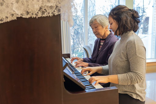 Teenaged Eurasian granddaughter playing piano with her grandmother.  Vancouver, British Columbia, Canada