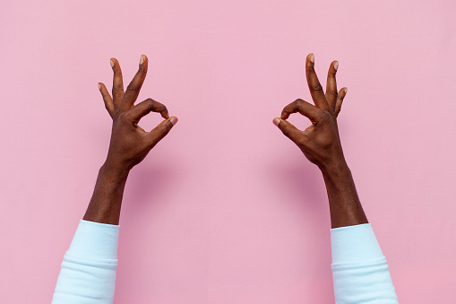 african american male hands show ok sign on pink isolated background, closeup