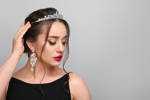 Beautiful young woman wearing luxurious tiara on light grey background, space for text