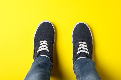 Child in stylish sneakers standing on yellow background, top view