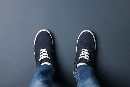 Child in stylish sneakers standing on grey background, top view