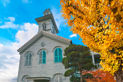 kyushu, japan - dec 14 2022: Two-story wooden building that has been preserved from Dejima Seminary built in 1877 for the New Christian Church in Nagasaki with a Ginkgo biloba below blue sky in autumn