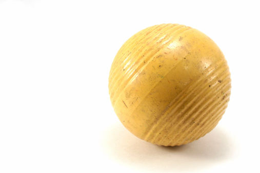 Old yellow croquet ball against a white background