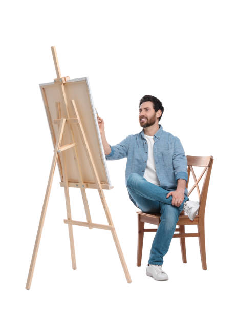 istock Happy man painting with brush against white background. Using easel to hold canvas 1721254422
