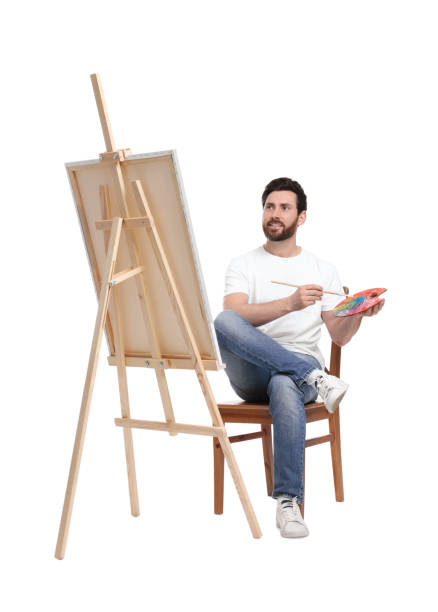 istock Man with brush painting against white background. Using easel to hold canvas 1721254424