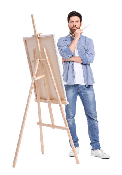 istock Man painting with brush against white background. Using easel to hold canvas 1721254441