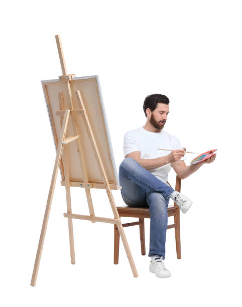 istock Man with brush painting against white background. Using easel to hold canvas 1721254966