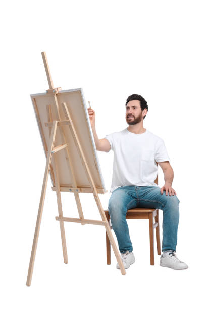 istock Man painting with brush against white background. Using easel to hold canvas 1721254973