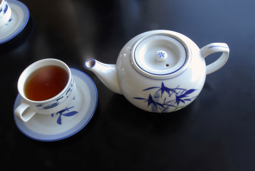 Steaming Chinese teapot, cup and saucer on black table.