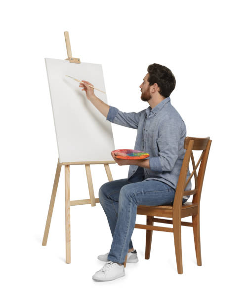 istock Man with brush painting against white background. Using easel to hold canvas 1721255494