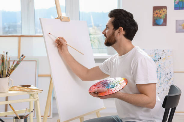 istock Man painting in studio. Using easel to hold canvas 1721256570