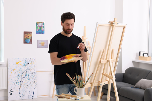 Senior artist holding a paintbrush and posing next to a canvas isolated on white background